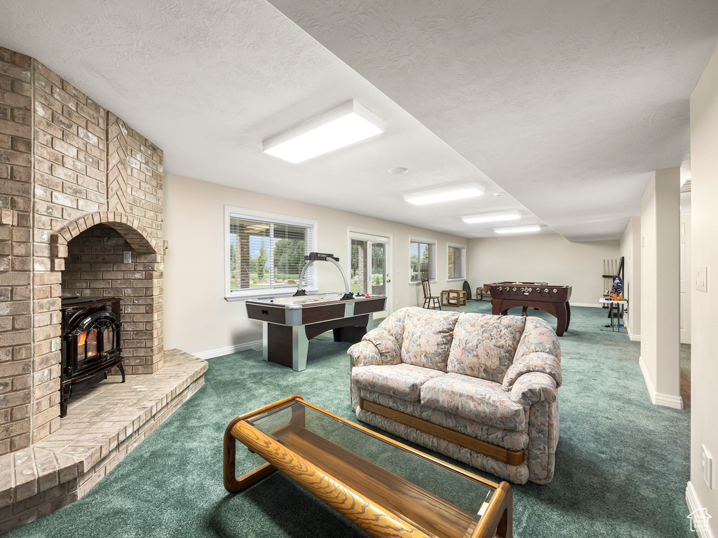 Living room with brick wall, dark colored carpet, a brick fireplace, and a textured ceiling