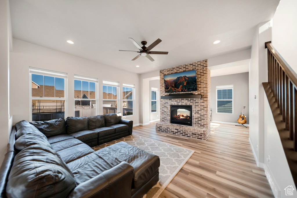 Living room with light wood-type flooring, brick wall, a brick fireplace, and ceiling fan