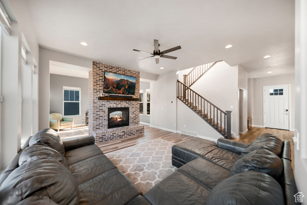 Living room with brick wall, light hardwood / wood-style floors, ceiling fan, and a brick fireplace