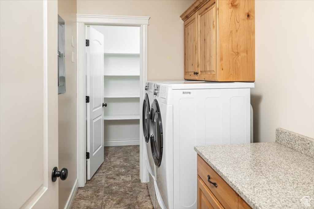 Clothes washing area featuring washer and clothes dryer, dark tile flooring, and cabinets