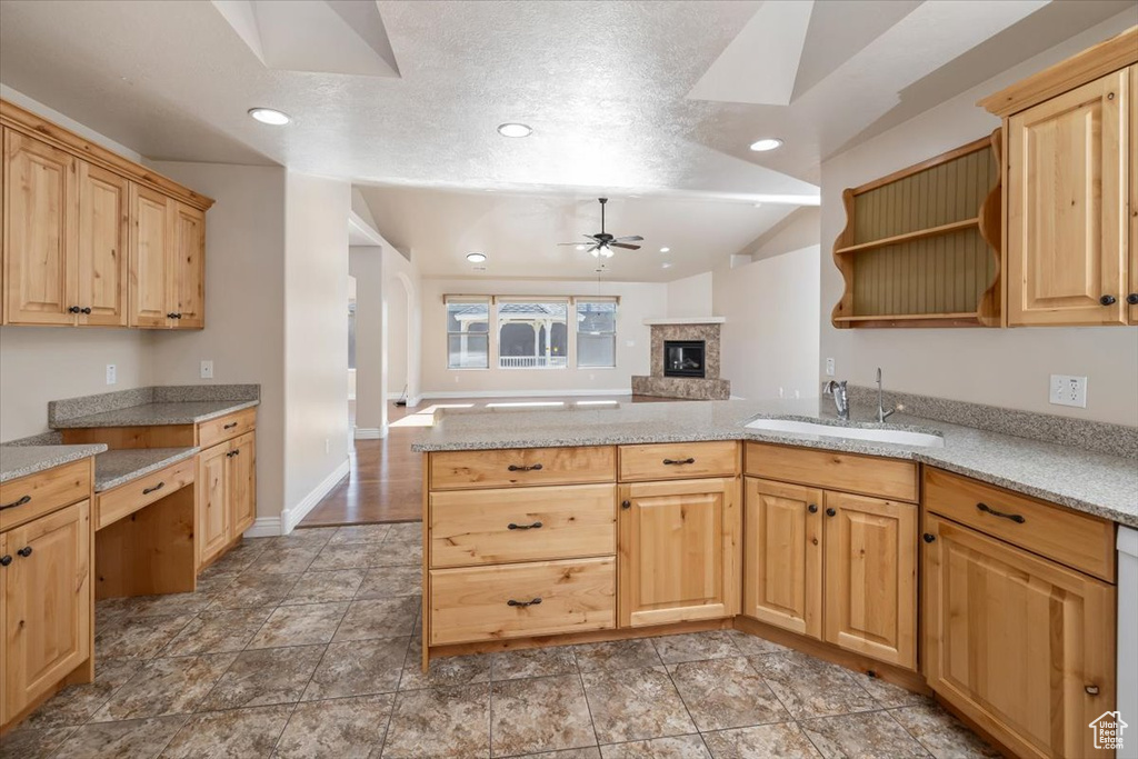 Kitchen featuring light stone counters, light brown cabinetry, ceiling fan, vaulted ceiling, and sink