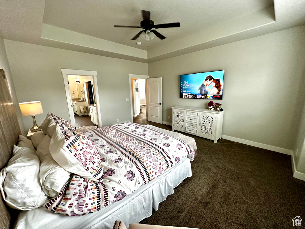 Bedroom with dark colored carpet, a raised ceiling, and ceiling fan