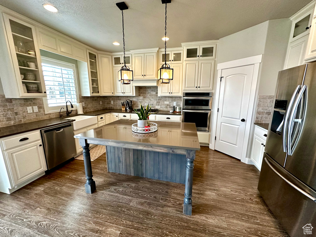 Kitchen featuring dark hardwood / wood-style flooring, stainless steel appliances, backsplash, hanging light fixtures, and a center island