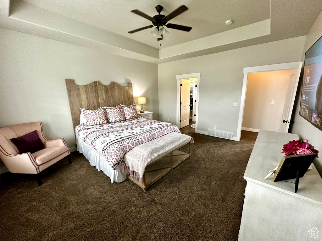Carpeted bedroom featuring a raised ceiling and ceiling fan