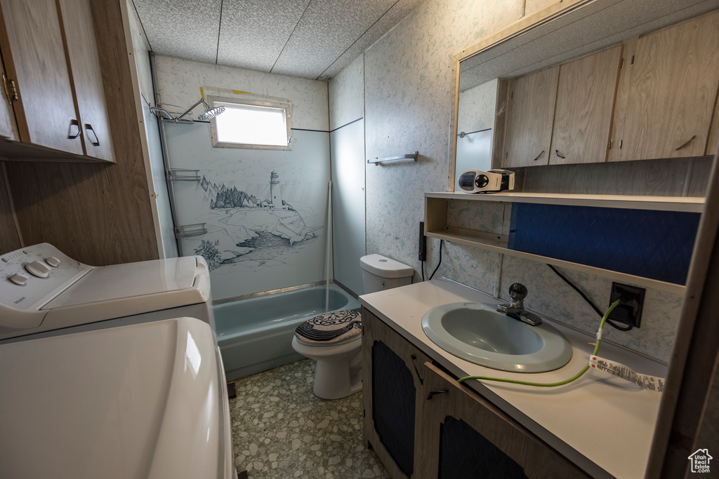Full bathroom with washing machine and clothes dryer, toilet, large vanity, tile floors, and bathtub / shower combination