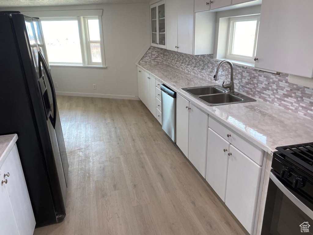 Kitchen featuring light hardwood / wood-style flooring, white cabinets, tasteful backsplash, sink, and black fridge with ice dispenser