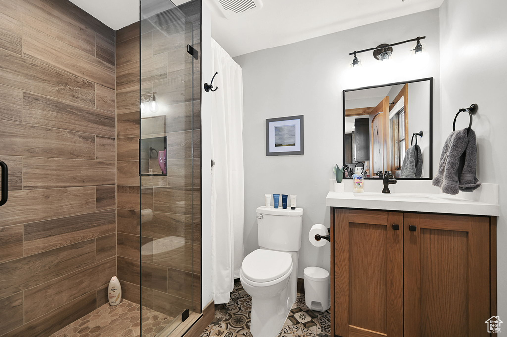Bathroom with a shower with shower door, toilet, vanity, and tile flooring