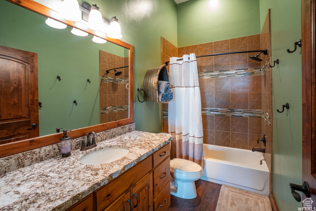 Full bathroom featuring hardwood / wood-style floors, shower / tub combo with curtain, toilet, and vanity with extensive cabinet space