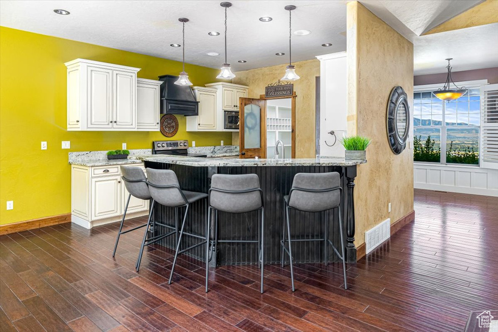 Kitchen with dark hardwood / wood-style floors, kitchen peninsula, custom exhaust hood, light stone countertops, and stainless steel microwave