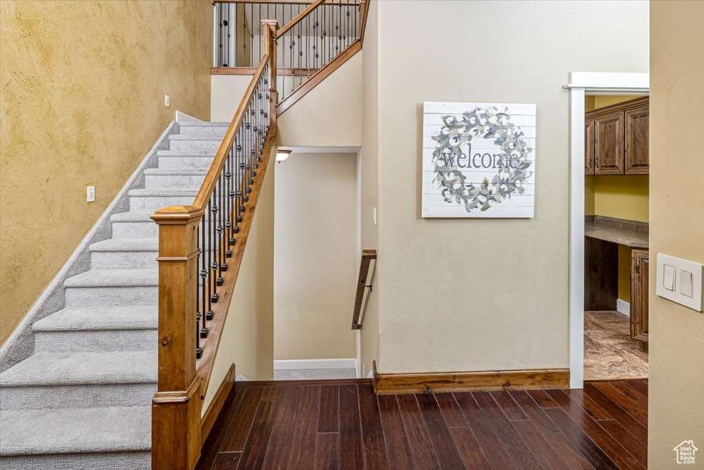 Staircase with a towering ceiling and wood-type flooring