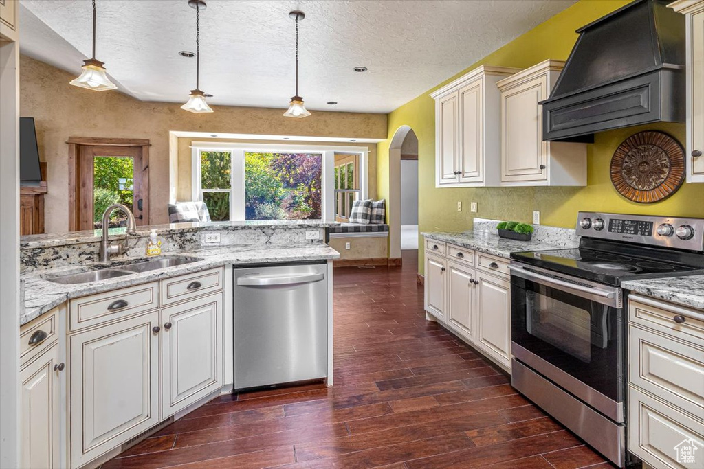 Kitchen featuring hanging light fixtures, dark wood-type flooring, stainless steel appliances, premium range hood, and sink