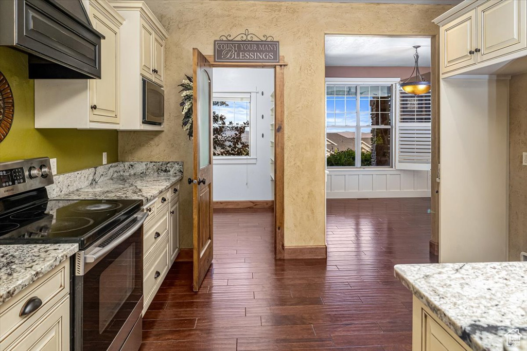 Kitchen featuring dark wood-type flooring, appliances with stainless steel finishes, light stone countertops, and cream cabinets