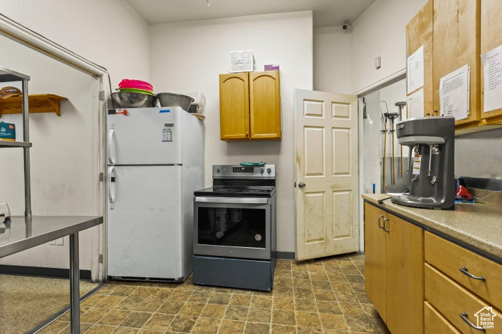 Kitchen with dark tile floors, white refrigerator, and stainless steel range with electric stovetop
