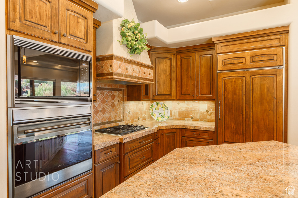Kitchen with built in appliances, custom range hood, light stone counters, and backsplash