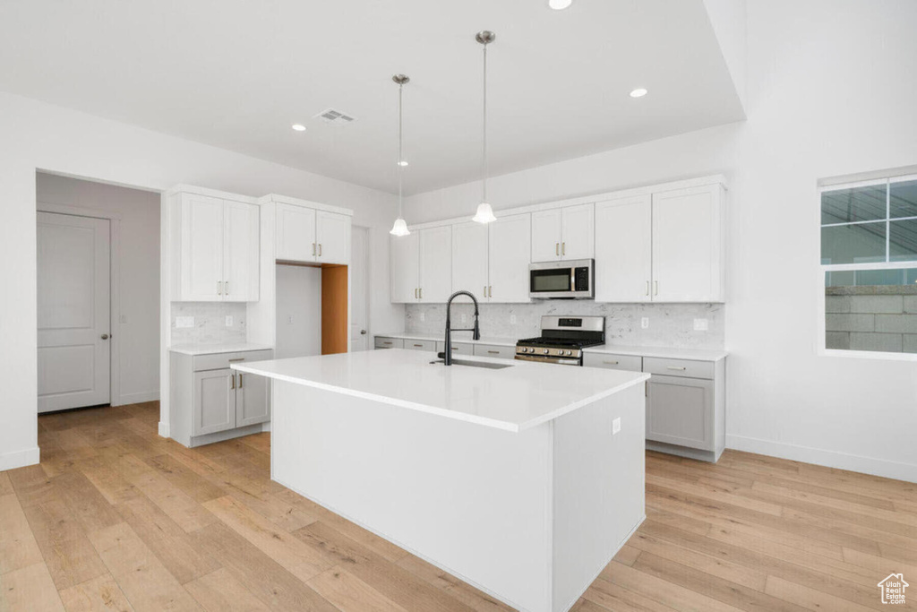 Kitchen featuring a center island with sink, white cabinets, hanging light fixtures, sink, and appliances with stainless steel finishes