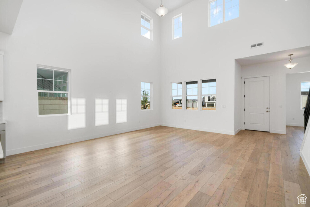 Unfurnished living room with a wealth of natural light, light hardwood / wood-style flooring, and a high ceiling