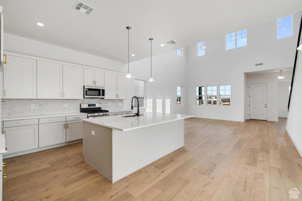 Kitchen featuring a center island with sink, light wood-type flooring, white cabinetry, tasteful backsplash, and appliances with stainless steel finishes