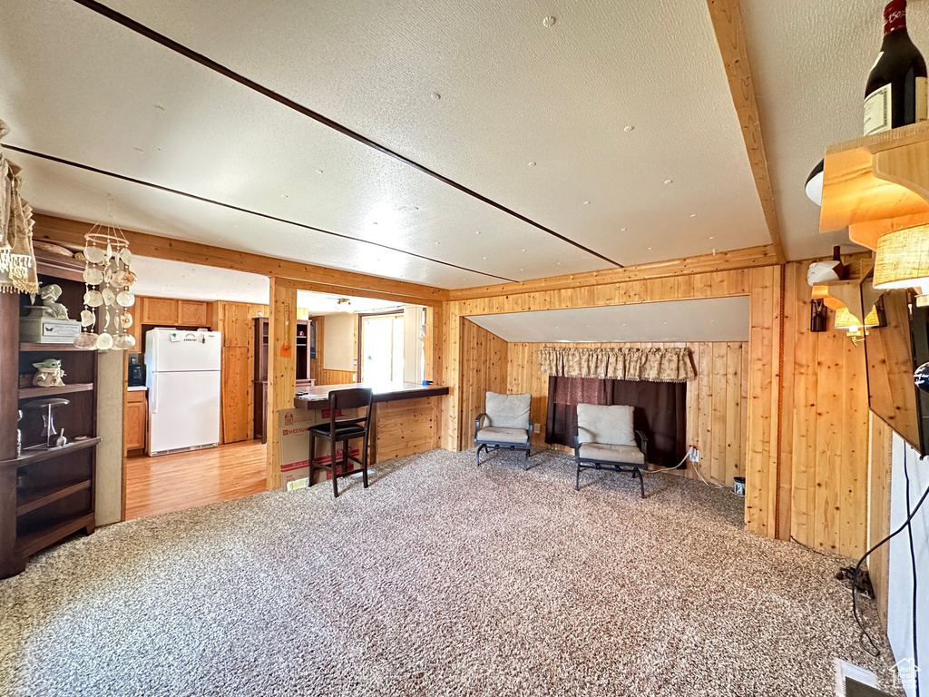 Interior space featuring wooden walls, beam ceiling, light colored carpet, and a textured ceiling