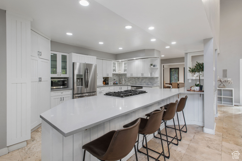 Kitchen with backsplash, white cabinets, a breakfast bar, light tile floors, and appliances with stainless steel finishes