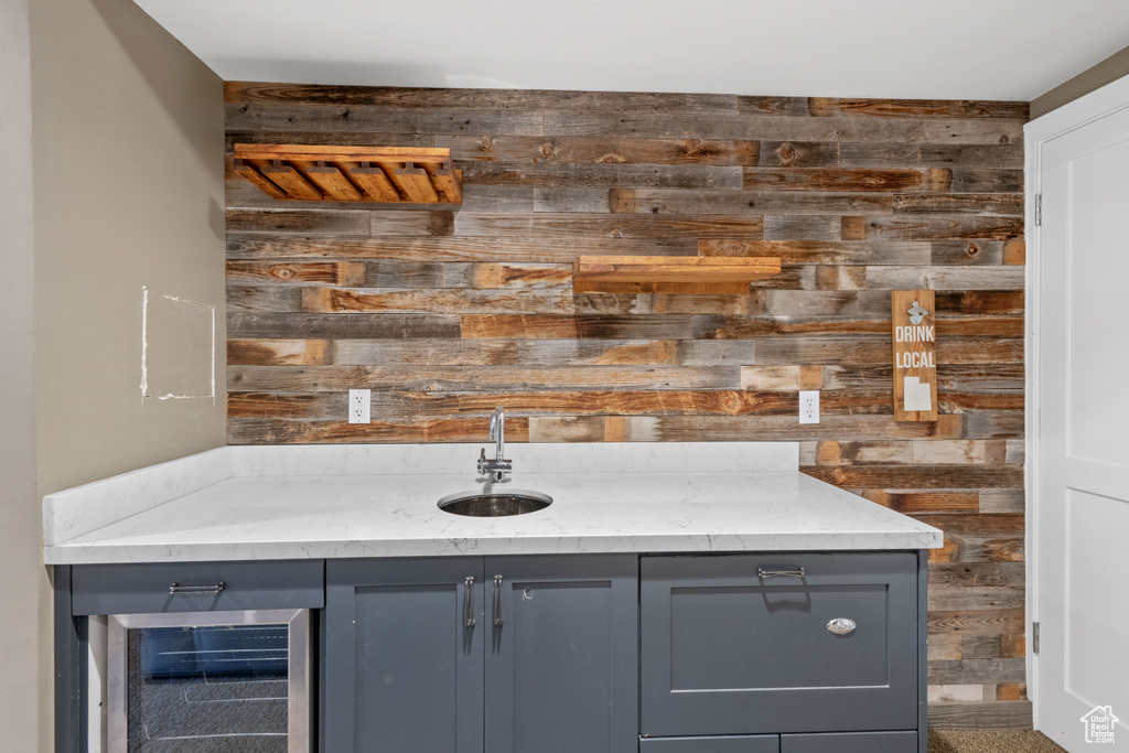 Bar featuring wooden walls, beverage cooler, and gray cabinetry