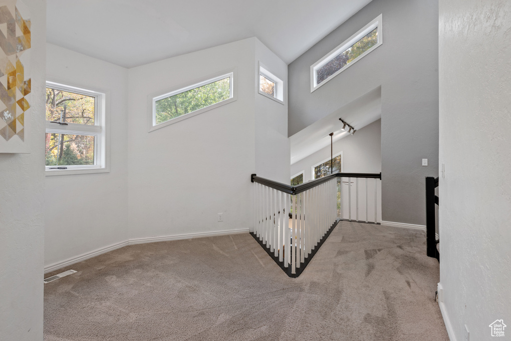 Staircase featuring an inviting chandelier, a wealth of natural light, light carpet, and a towering ceiling