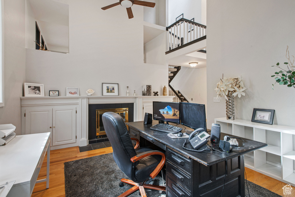 Office featuring light hardwood / wood-style floors, a towering ceiling, ceiling fan, and a tile fireplace