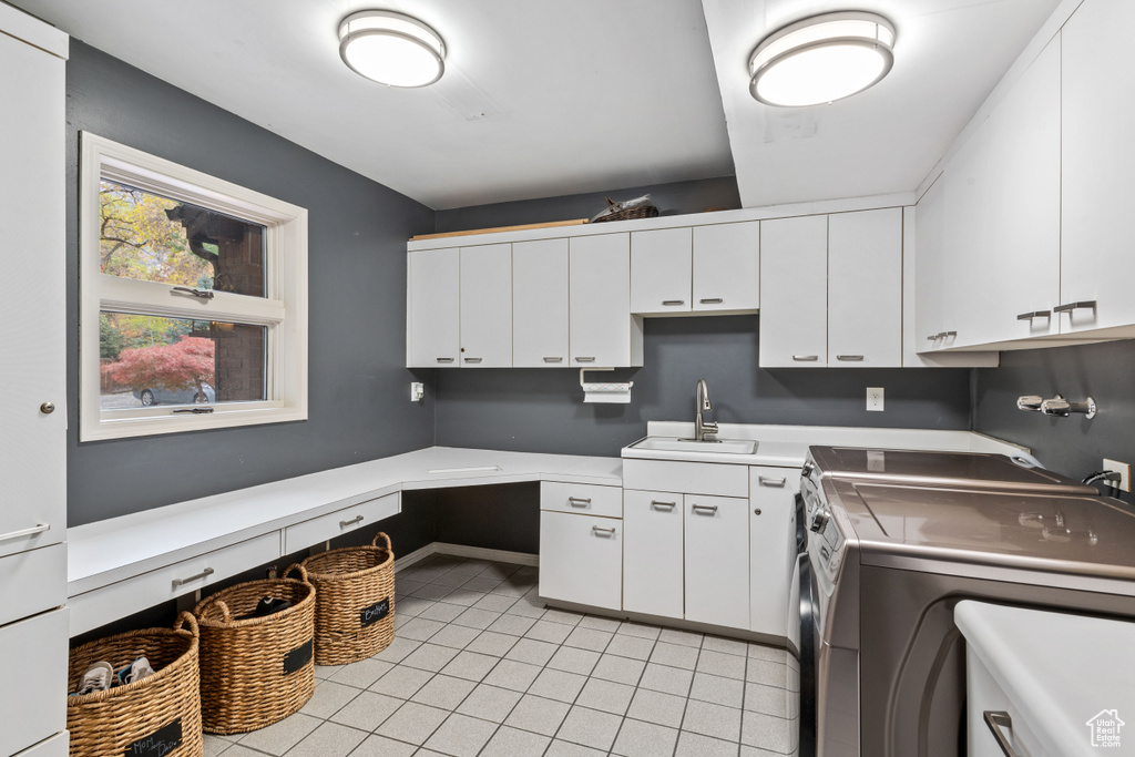 Kitchen with white cabinets, sink, washing machine and dryer, and light tile floors