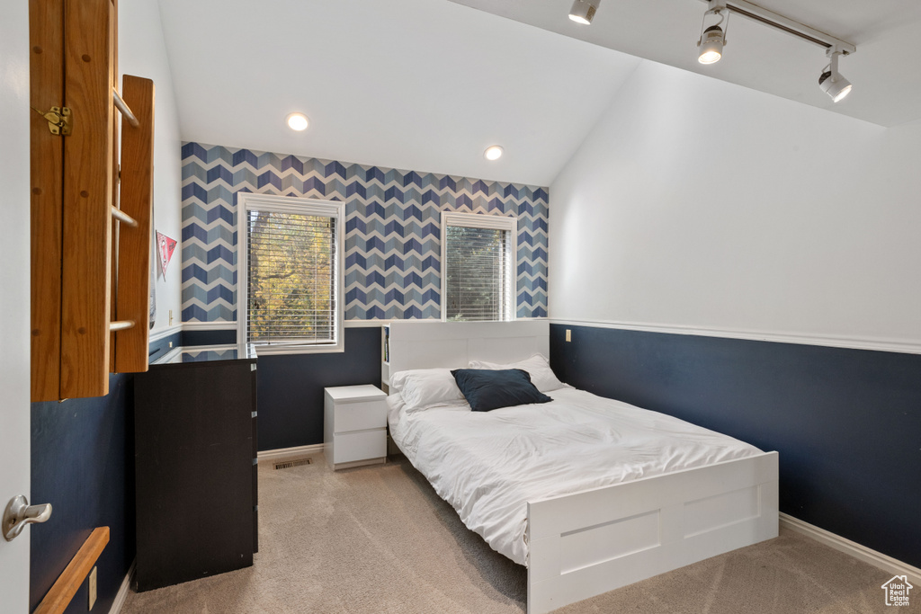 Carpeted bedroom featuring rail lighting and lofted ceiling