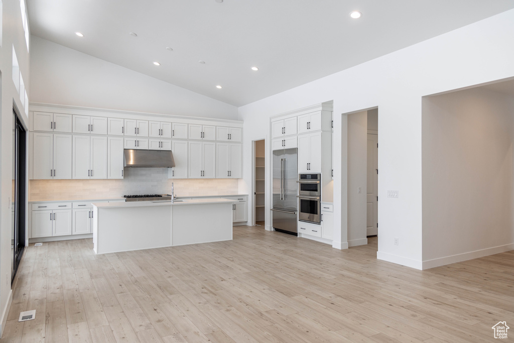 Kitchen with a kitchen island with sink, white cabinets, light wood-type flooring, and tasteful backsplash