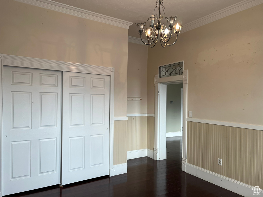 Unfurnished bedroom featuring an inviting chandelier, dark hardwood / wood-style flooring, ornamental molding, and a closet