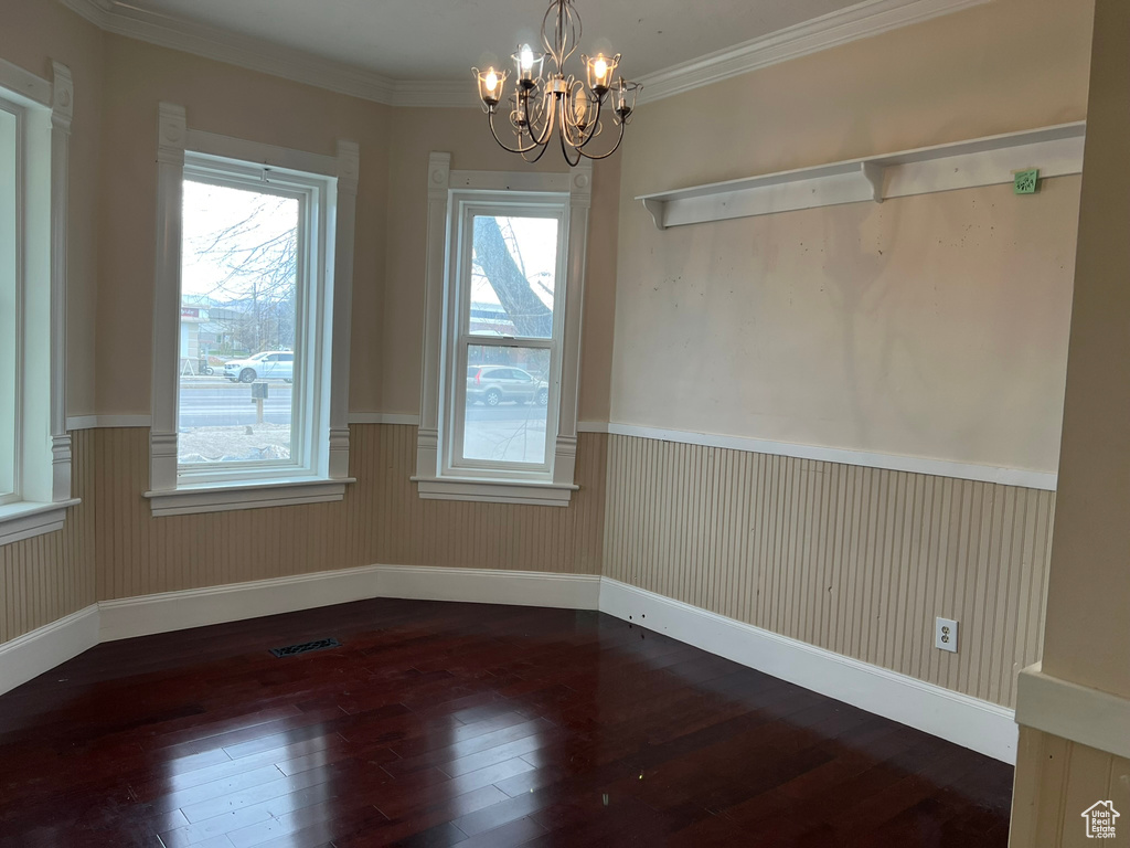 Empty room with an inviting chandelier, crown molding, and dark wood-type flooring