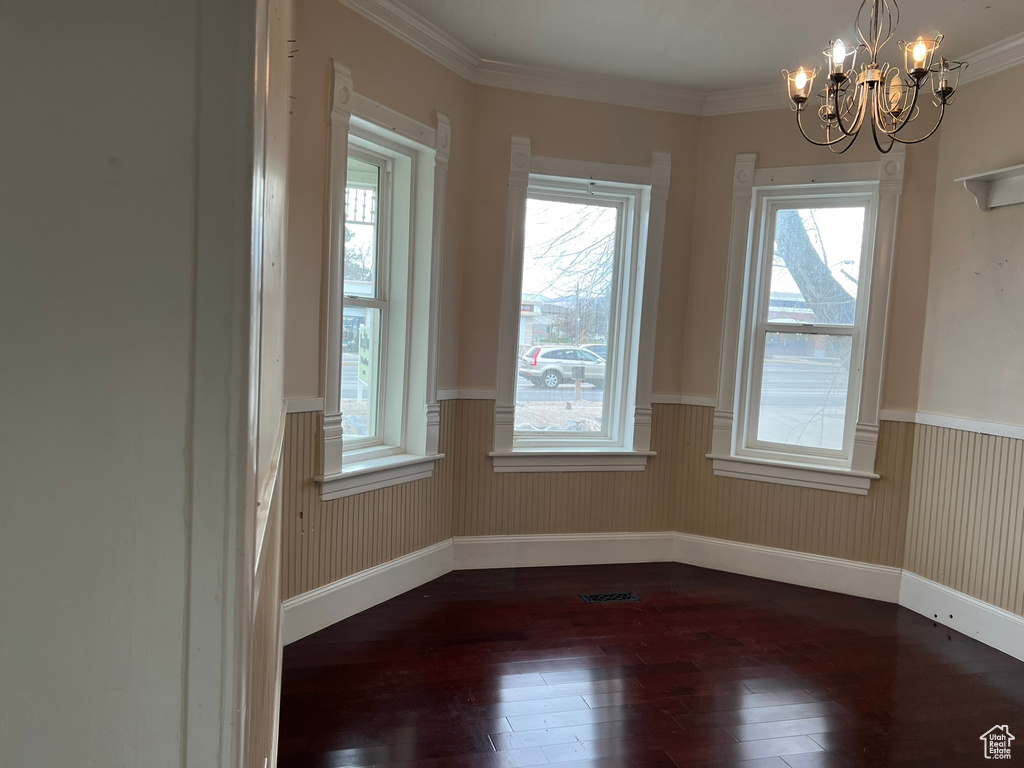 Spare room featuring plenty of natural light, dark hardwood / wood-style flooring, a notable chandelier, and ornamental molding