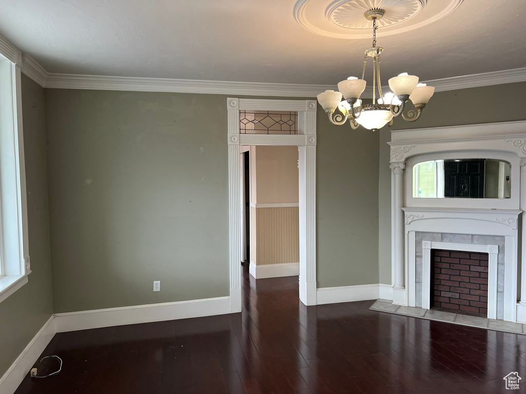 Unfurnished living room featuring dark hardwood / wood-style flooring, crown molding, and a notable chandelier