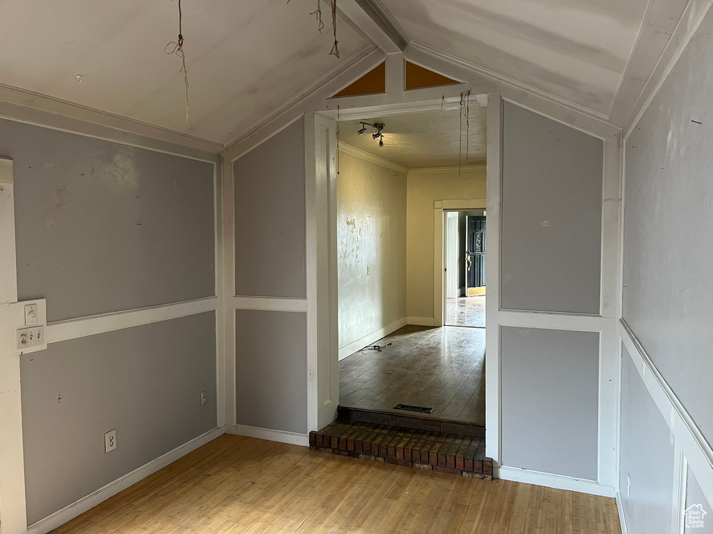 Empty room featuring vaulted ceiling with beams, ornamental molding, and light wood-type flooring