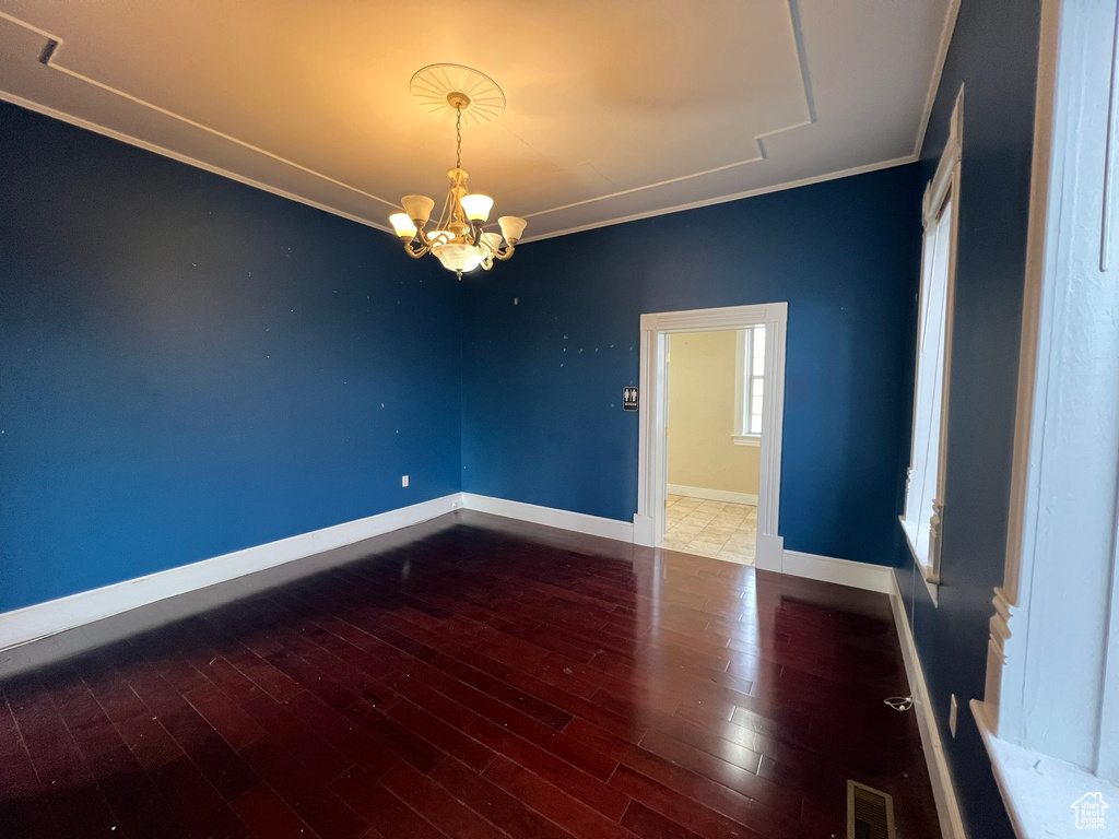 Spare room with dark hardwood / wood-style floors, a chandelier, and ornamental molding
