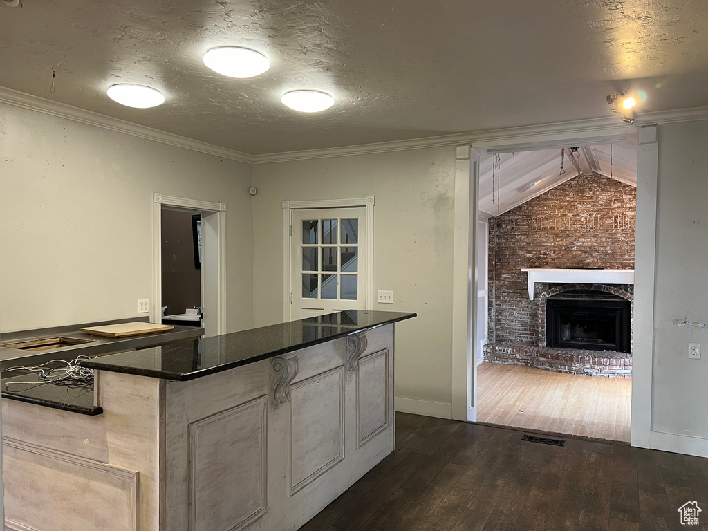Kitchen featuring brick wall, crown molding, a brick fireplace, dark hardwood / wood-style flooring, and dark stone countertops