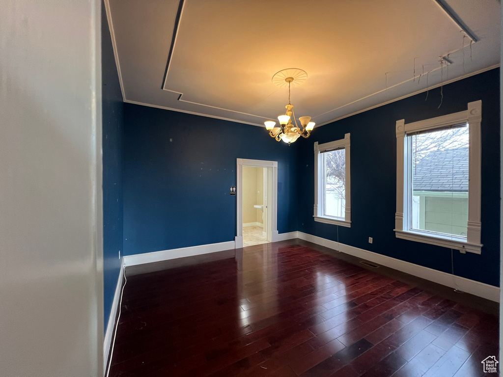 Unfurnished room featuring dark wood-type flooring, a notable chandelier, and ornamental molding