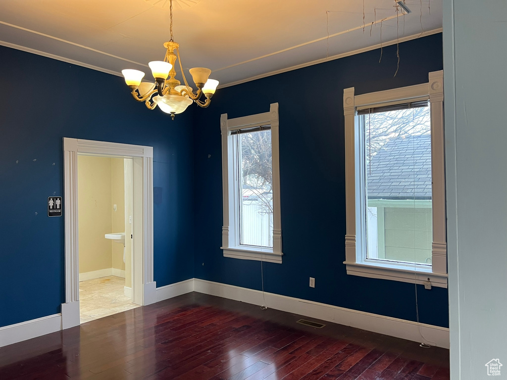 Unfurnished room featuring dark hardwood / wood-style flooring, crown molding, a chandelier, and a healthy amount of sunlight