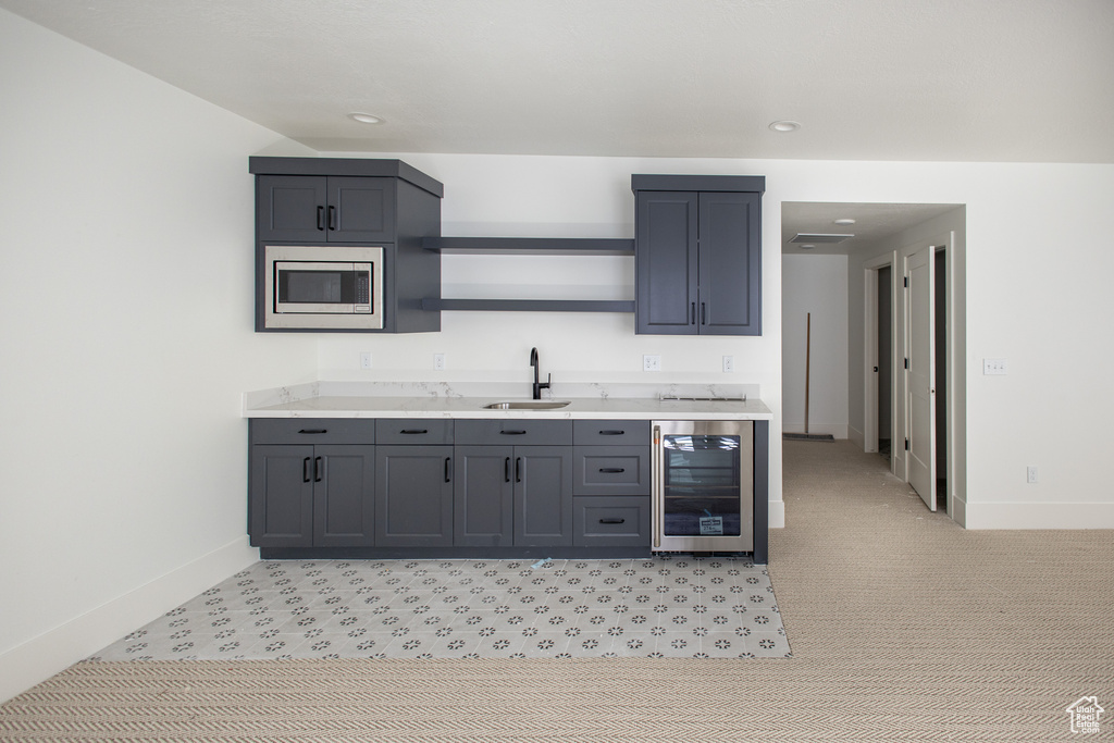 Kitchen with wine cooler, light carpet, gray cabinetry, stainless steel microwave, and sink