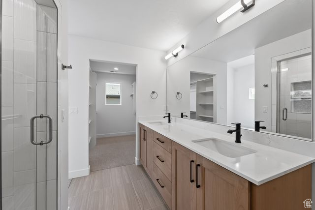 Bathroom with a shower with shower door, tile flooring, large vanity, and double sink