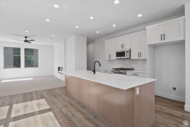 Kitchen featuring light hardwood / wood-style flooring, stove, ceiling fan, tasteful backsplash, and an island with sink