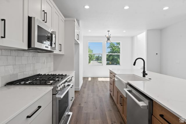 Kitchen featuring white cabinetry, hanging light fixtures, stainless steel appliances, hardwood / wood-style flooring, and backsplash