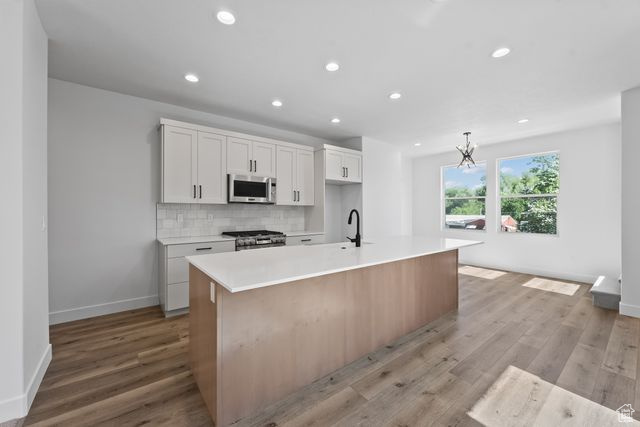 Kitchen with light hardwood / wood-style floors, tasteful backsplash, range, a kitchen island with sink, and white cabinets