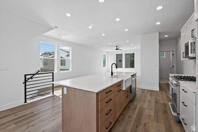 Kitchen with white cabinets, appliances with stainless steel finishes, an island with sink, and hardwood / wood-style floors