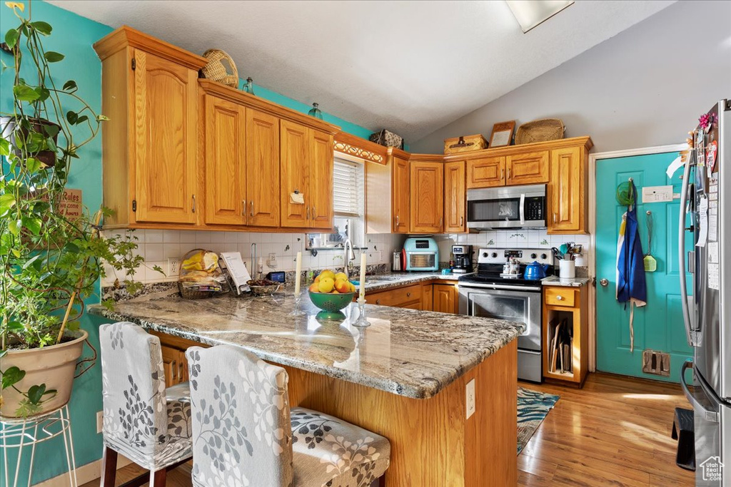 Kitchen featuring light hardwood / wood-style flooring, light stone countertops, vaulted ceiling, tasteful backsplash, and stainless steel appliances