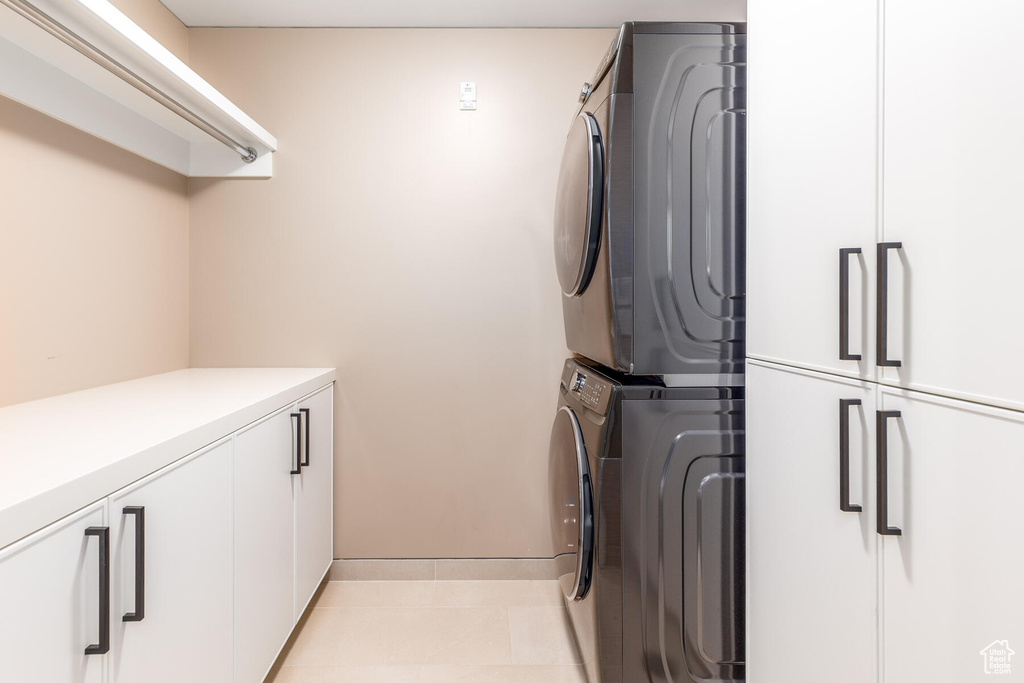 Washroom featuring cabinets, light tile floors, and stacked washer / dryer