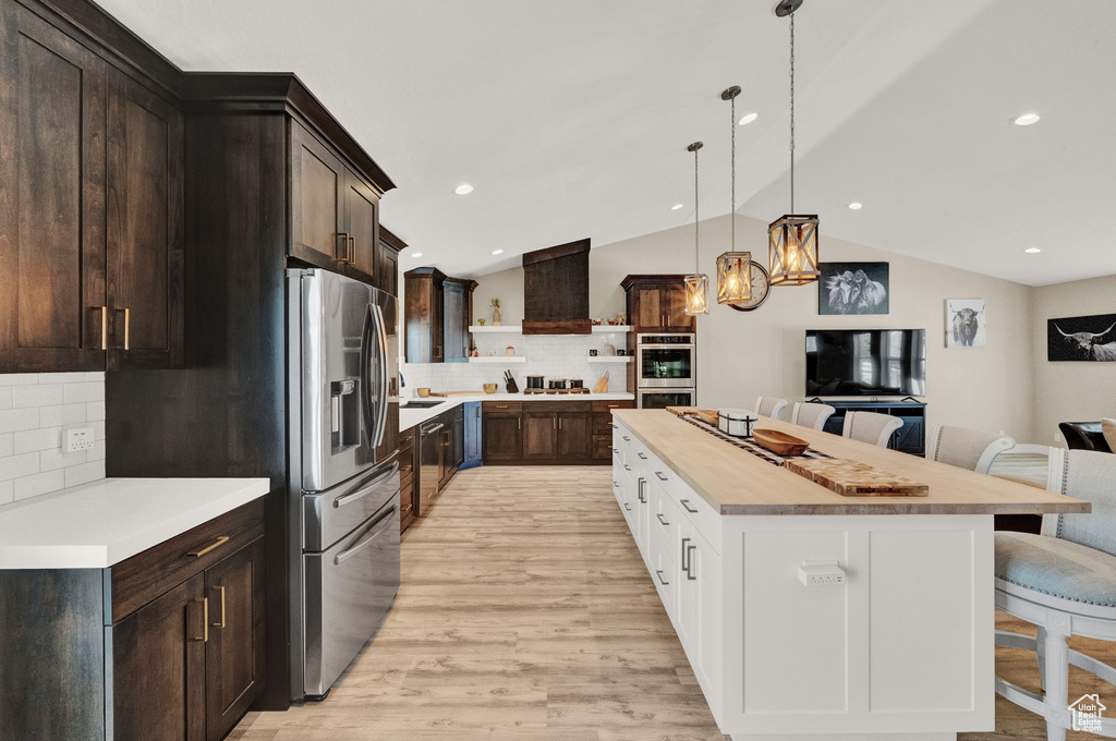 Kitchen with light hardwood / wood-style flooring, backsplash, a kitchen bar, vaulted ceiling, and appliances with stainless steel finishes