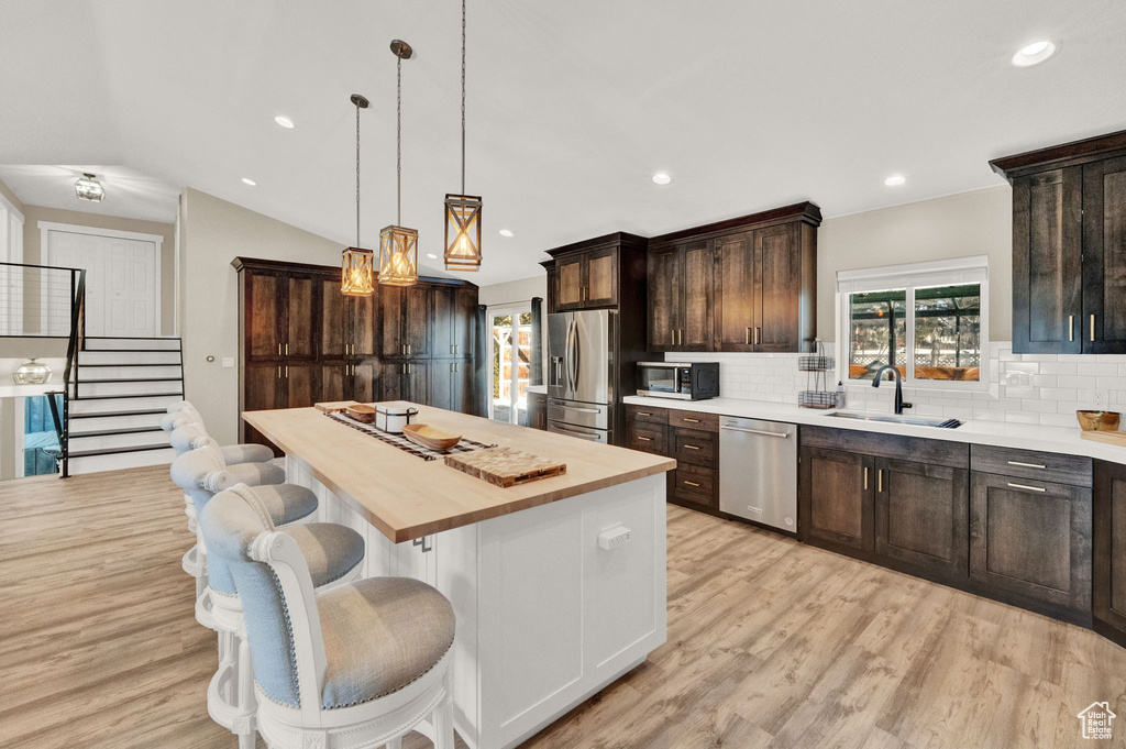 Kitchen featuring tasteful backsplash, stainless steel appliances, vaulted ceiling, and light wood-type flooring
