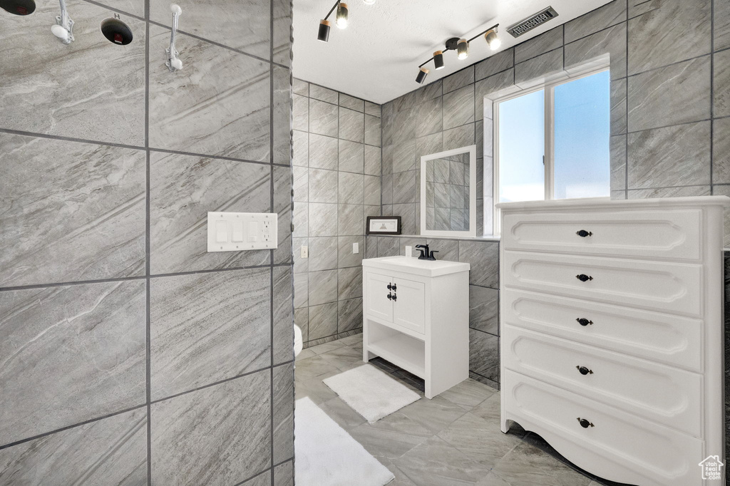 Bathroom with rail lighting, vanity, tile walls, a tile shower, and tile floors