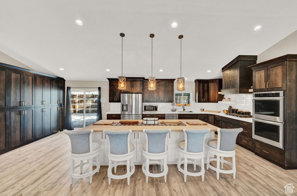Kitchen featuring a kitchen island, custom range hood, appliances with stainless steel finishes, light hardwood / wood-style flooring, and lofted ceiling